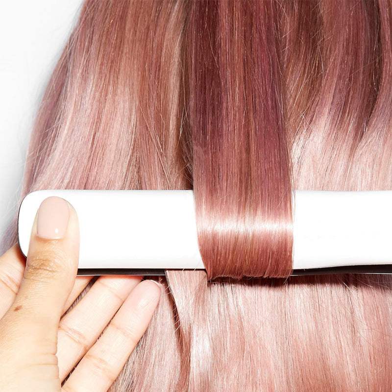 Ceramic Hair Straightener with white casing smoothing a section of long pink-toned hair