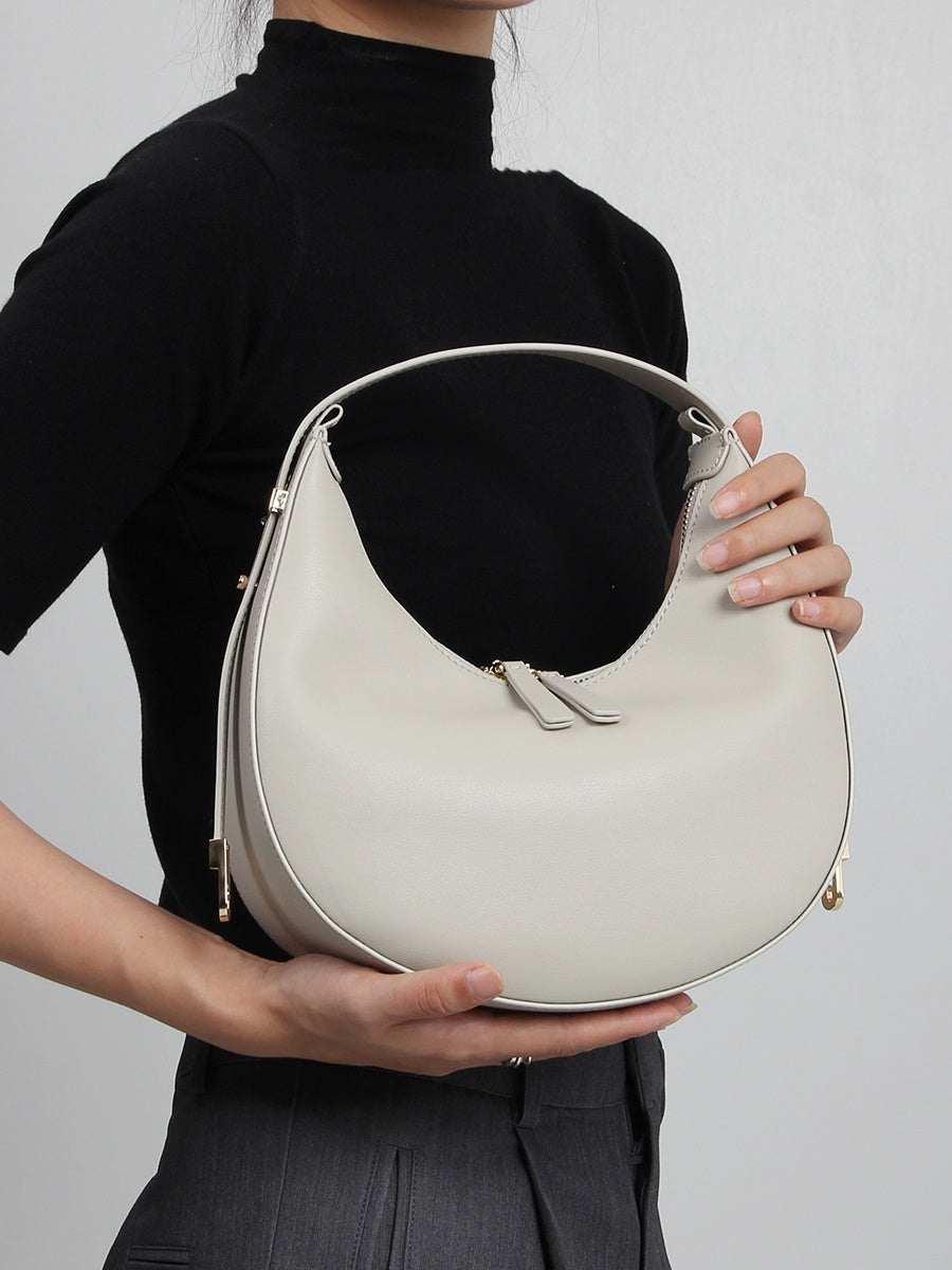 Cowhide Crossbody Bag in pale grey-white leather with a smooth finish, curved silhouette, zip closure and jointed strap