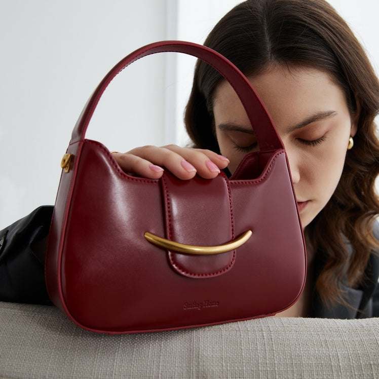 Red Cowhide Occasion Bag in smooth burgundy leather, with a curved top handle, stitched panels and gold-tone bar detail