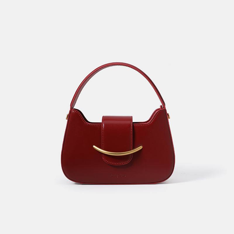 Red Cowhide Occasion Bag with a smooth burgundy-red finish, curved silhouette, top handle and gold-tone curved accent